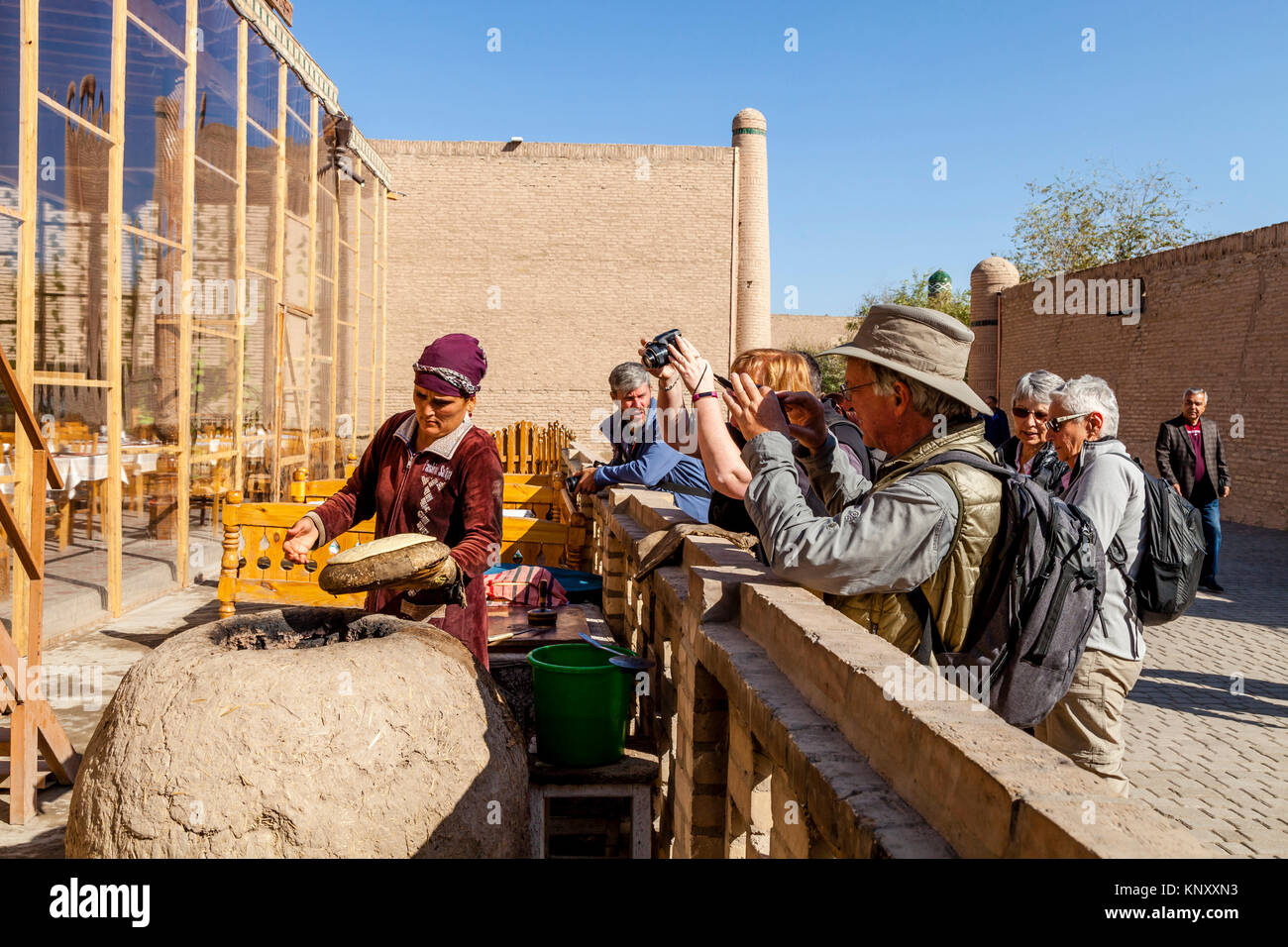 Eine lokale Frau backt Brot in einem traditionellen Lehmofen beobachtete eine Gruppe von Touristen, Chiwa, Usbekistan Stockfoto