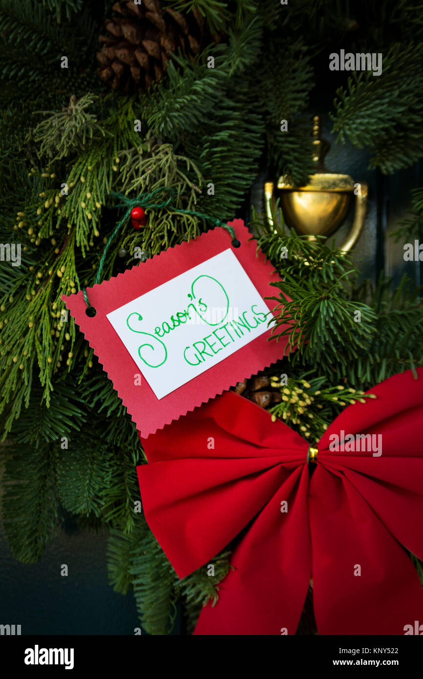 Weihnachten Kranz auf Tür mit roter Schleife und 'season's Greetings' Meldung Stockfoto