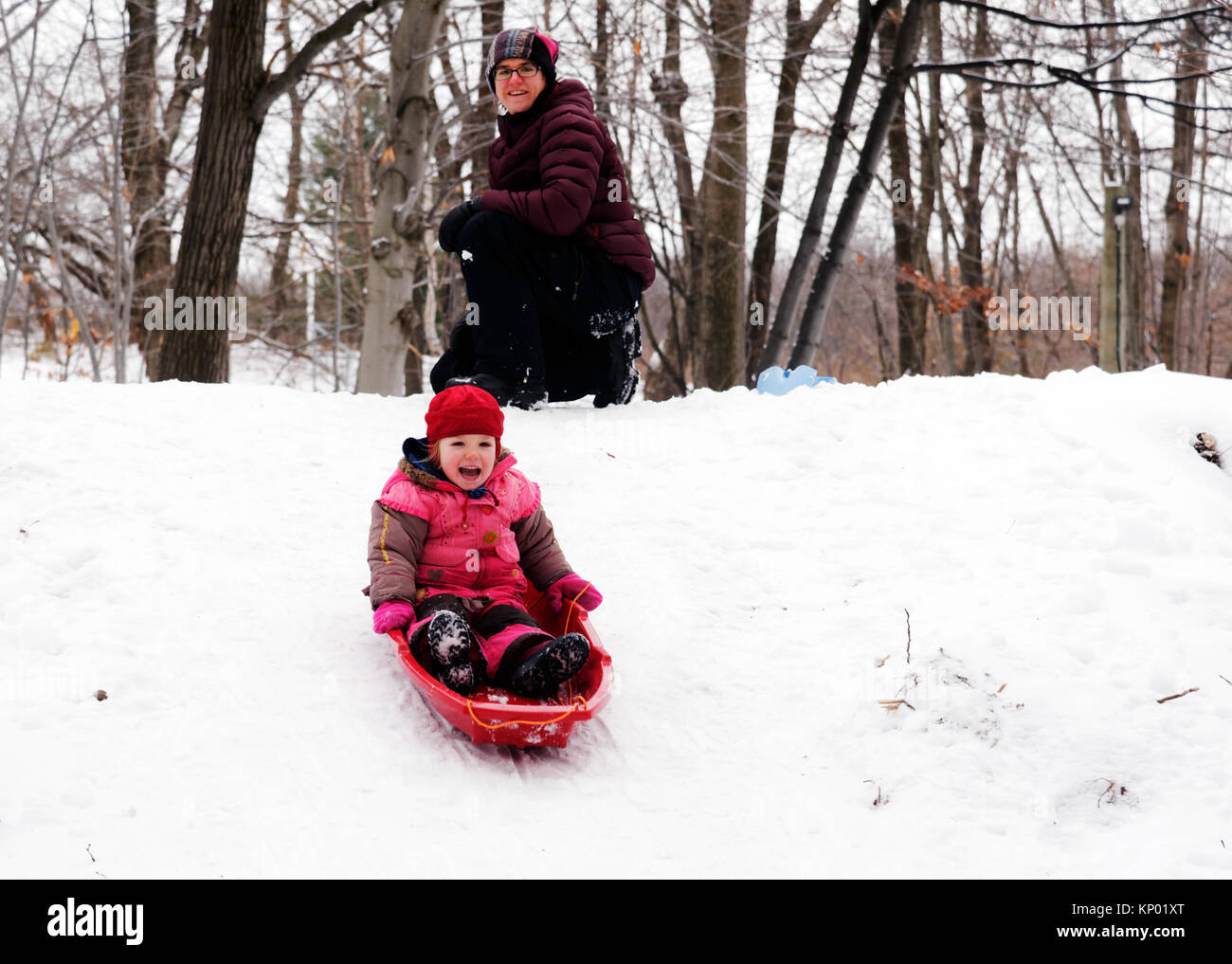 Ein kleines Mädchen (3 Jahre alt) Rodeln in Quebec, während Mama auf sieht Stockfoto