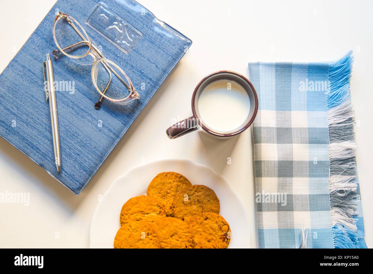 Notiz Buch, Brillen, Kugelschreiber, Schüssel, Cookies, Tasse Milch und Serviette. Stockfoto