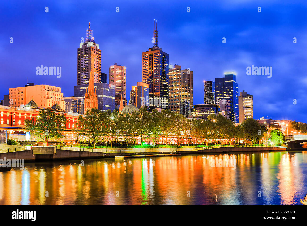 Blaue Dunkelheit über die Stadt Melbourne CBD überragt Flinders Bahnhof mit heller Beleuchtung in unscharfer Gewässern des Yarra River spiegeln. Stockfoto