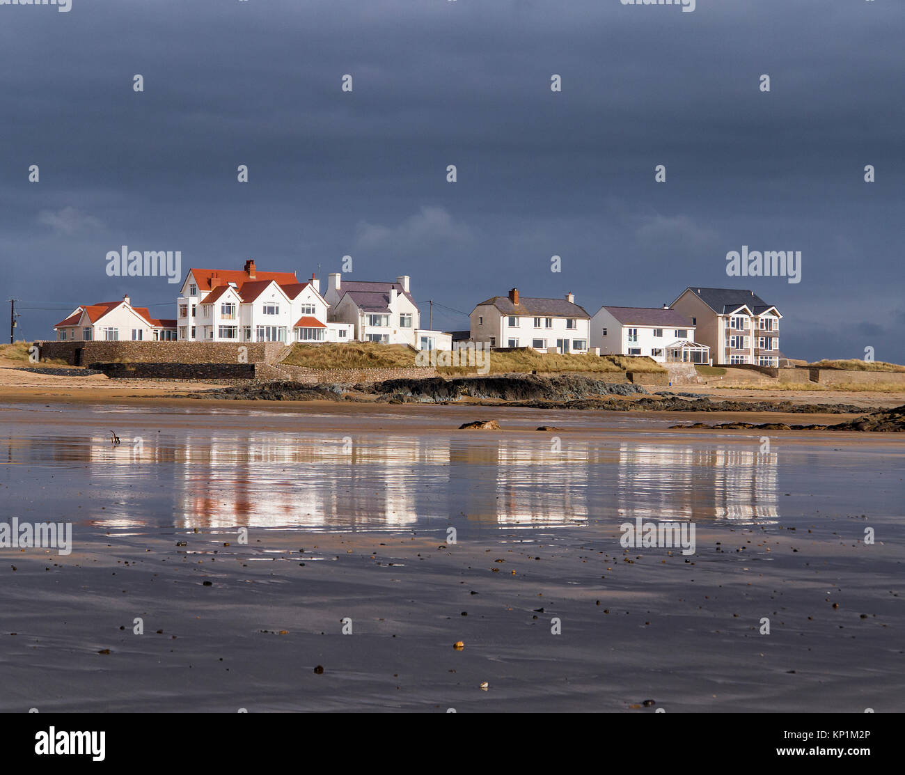 Eine Reihe von weißen Gebäude mit Blick auf das Wasser am breiten Strand in der Nähe von Rhosneigr auf Anglesey mit Reflexionen in den nassen Sand Stockfoto