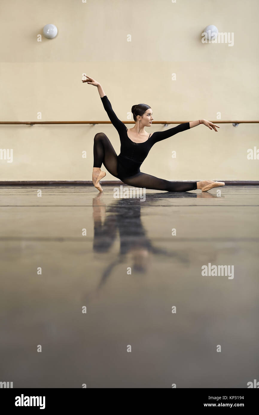 Erstaunlich Ballerina in der Hälfte Split auf der glänzenden Fußboden in der Dance Hall posieren. Sie schaut auf die Seite mit ausgestreckten Armen. Mädchen trägt ein schwarzes Dan Stockfoto