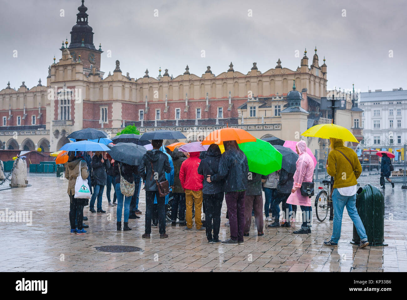 Touristen regen Schirme Europa, unter Sonnenschirmen im schweren Regen eine Reisegruppe lauschen ihren Führer im großen Marktplatz in Krakau, Polen. Stockfoto