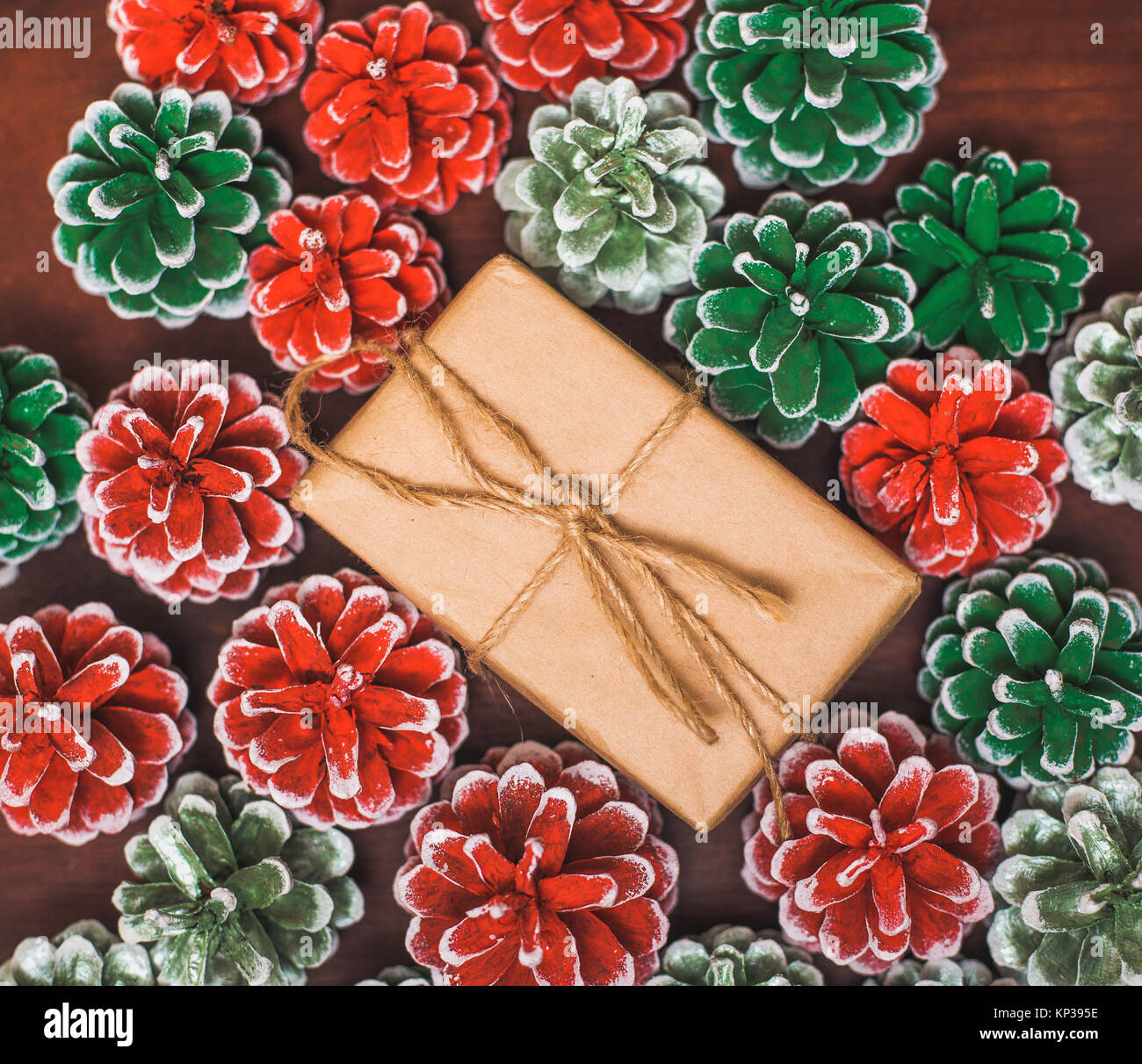 Weihnachten Hintergrund. Box in Braun craft Geschenkpapier mit Schleife und festlich lackiert rote und grüne Farbe tannenzapfen Stockfoto