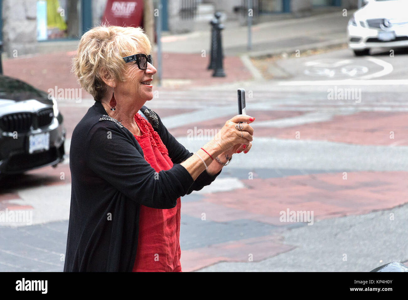 Vancouver, Kanada - August 31th, 2017: Eine ältere Frau ist das Aufnehmen von Fotos mit Ihrem mobilen trägt Prada Sonnenbrille auf der Straße in Vancouver. Stockfoto