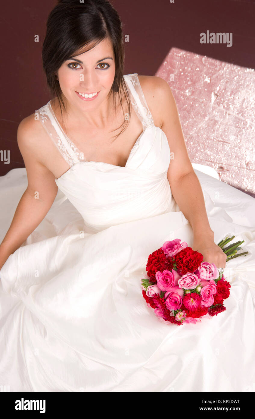 Braut Sitzen im weissen Brautkleid mit Blumenstrauß rote Rosen Stockfoto