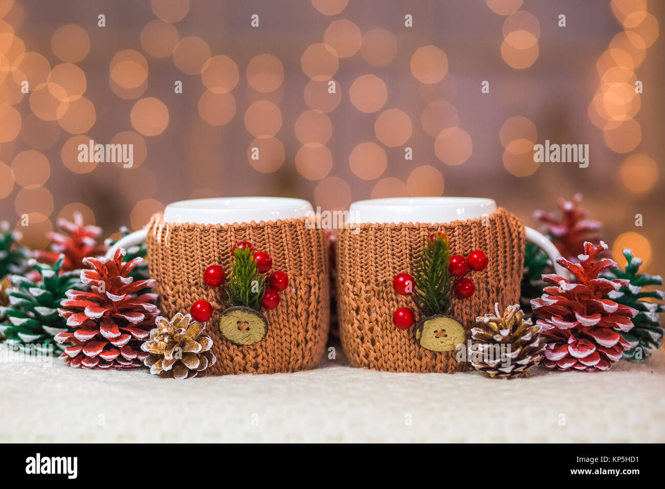Nahaufnahme von zwei weiße Tassen in Braun gestrickte Pullover mit weihnachtsschmuck an der Ampel von orange Girlande Hintergrund Stockfoto