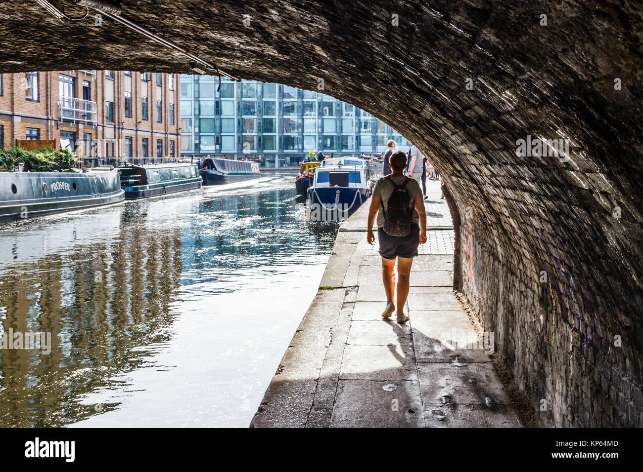 Eine Frau, die unter einer Brücke auf dem Leinpfad des Regent's Canal, London, UK bummeln Stockfoto