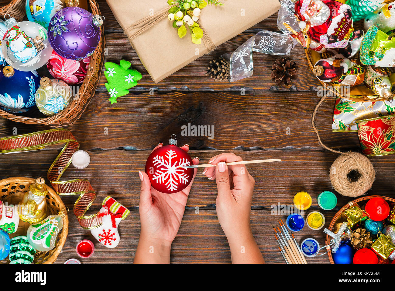 Weihnachtsschmuck, Bälle, Spielzeug und Geschenkboxen auf alten Holz- Board. Weibliche Hände zeichnen das neue Jahr Dekorationen. Schönen Rahmen mit freiem Speicherplatz. Idee fo Stockfoto