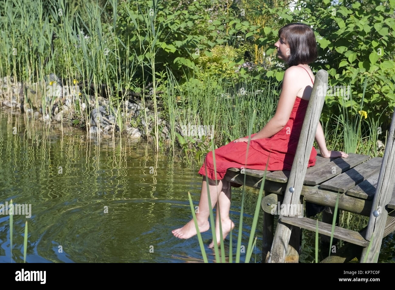 Model Release, Junge Frau Im Roten APPLELOVE Sitzt Auf Steg 'm Teich - junge Frau im roten Kleid sitzt auf einem Spaziergang an einem Teich Stockfoto