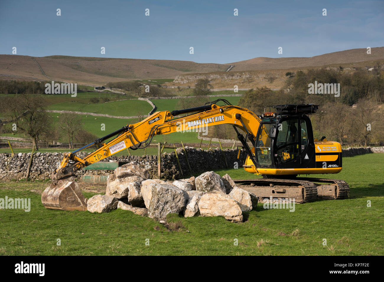 Hellgelb JCB JS130LC Raupenbagger steht auf dem Land Bauernhof Feld, bereit, schwere Felsbrocken heben - Kilnsey, Yorkshire Dales, England, UK. Stockfoto