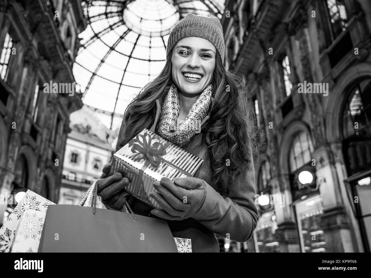 Auf einem riesigen Weihnachtsgeschäft in der italienischen Modehauptstadt. Portrait von glücklich elegante Reisende Frau mit Weihnachtsgeschenk und Einkaufstaschen in Mailand, Italien Stockfoto