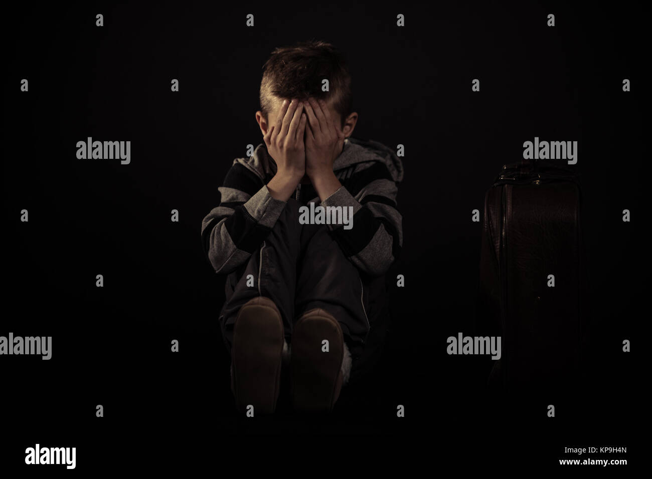 Sitzende Angst Junge bedeckte sein Gesicht gegen Schwarze Stockfoto