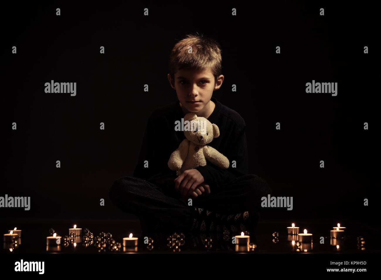Junge mit Teddybär sitzt auf dem Boden mit Kerzen Stockfoto