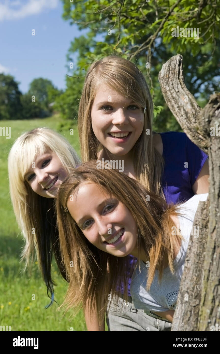 Model Release, Drei Jugendliche näher Schauen Hinter Baumstamm Hervor - drei Mädchen im Teenageralter außerhalb Stockfoto