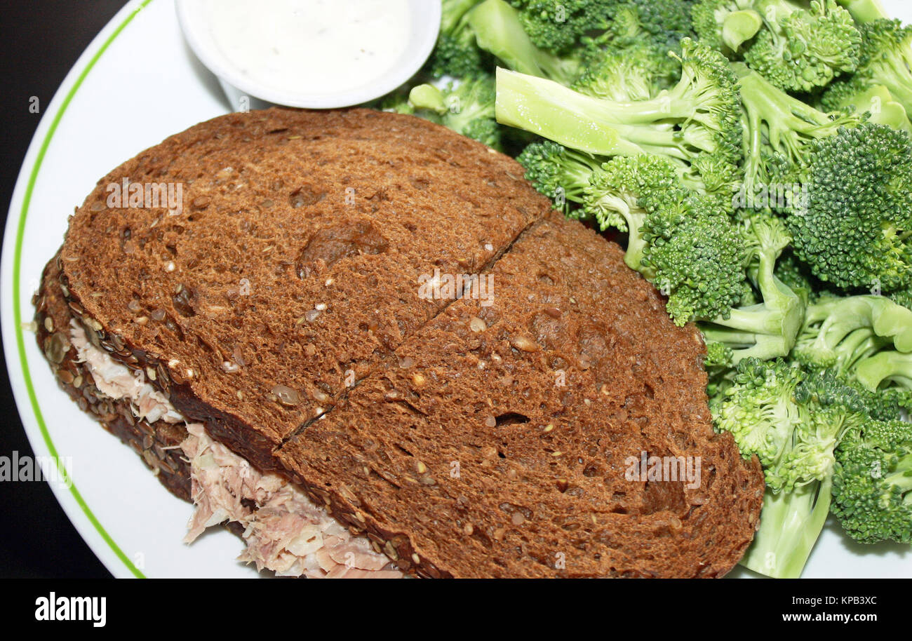 Thunfisch salat Sandwich auf dunkle Roggenbrot mit einer Seite der frischen, rohen Brokkoli und eine Soße Stockfoto