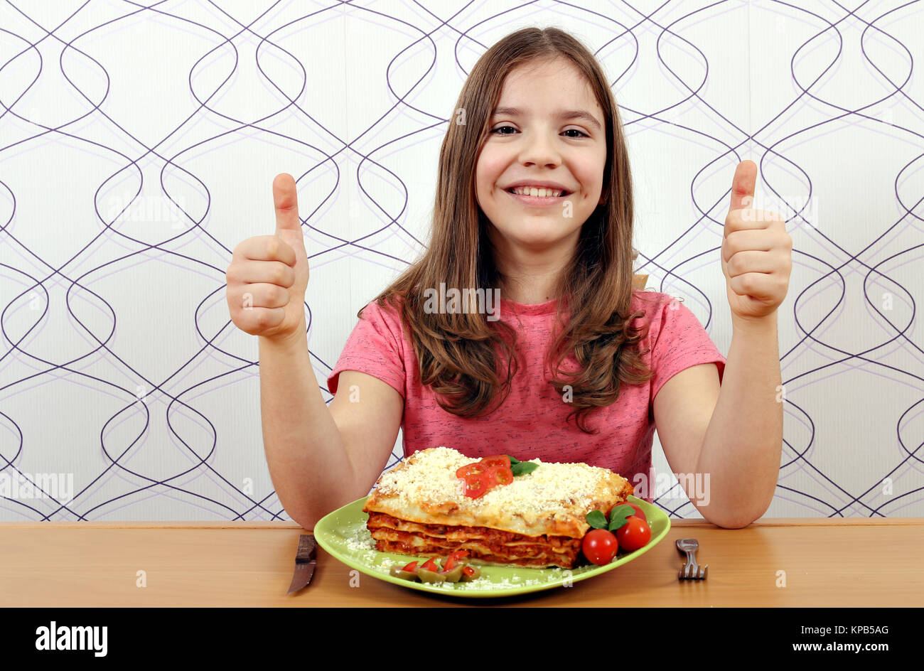 Glückliche kleine Mädchen mit Lasagne und Daumen hoch Stockfoto