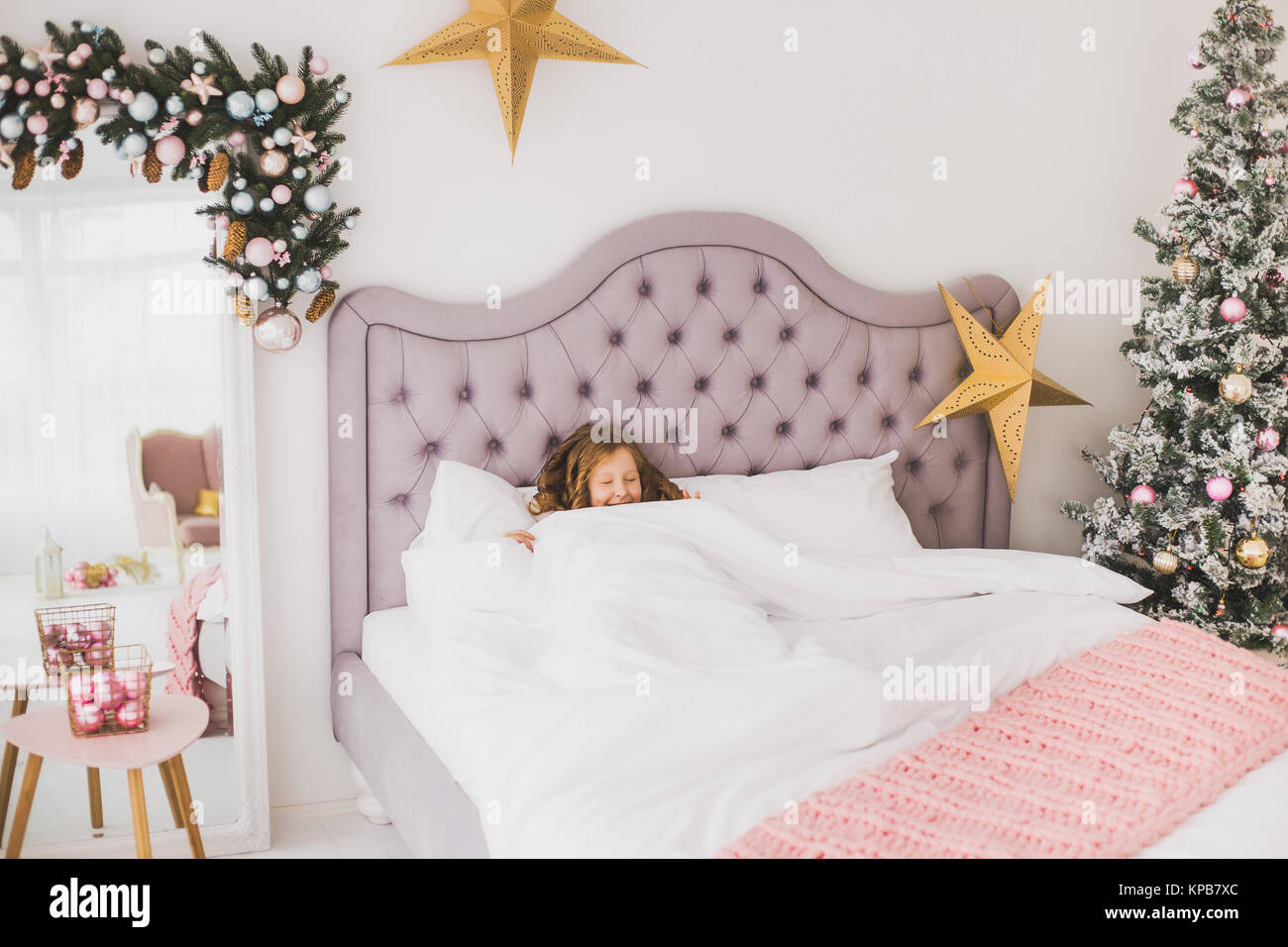 Portrait von niedlichen Lustige kleine Mädchen am Weihnachtsmorgen in Weiß Home Interior. Kind vorgibt zu schlafen als steigt fröhlich im Bett. Horizont Stockfoto