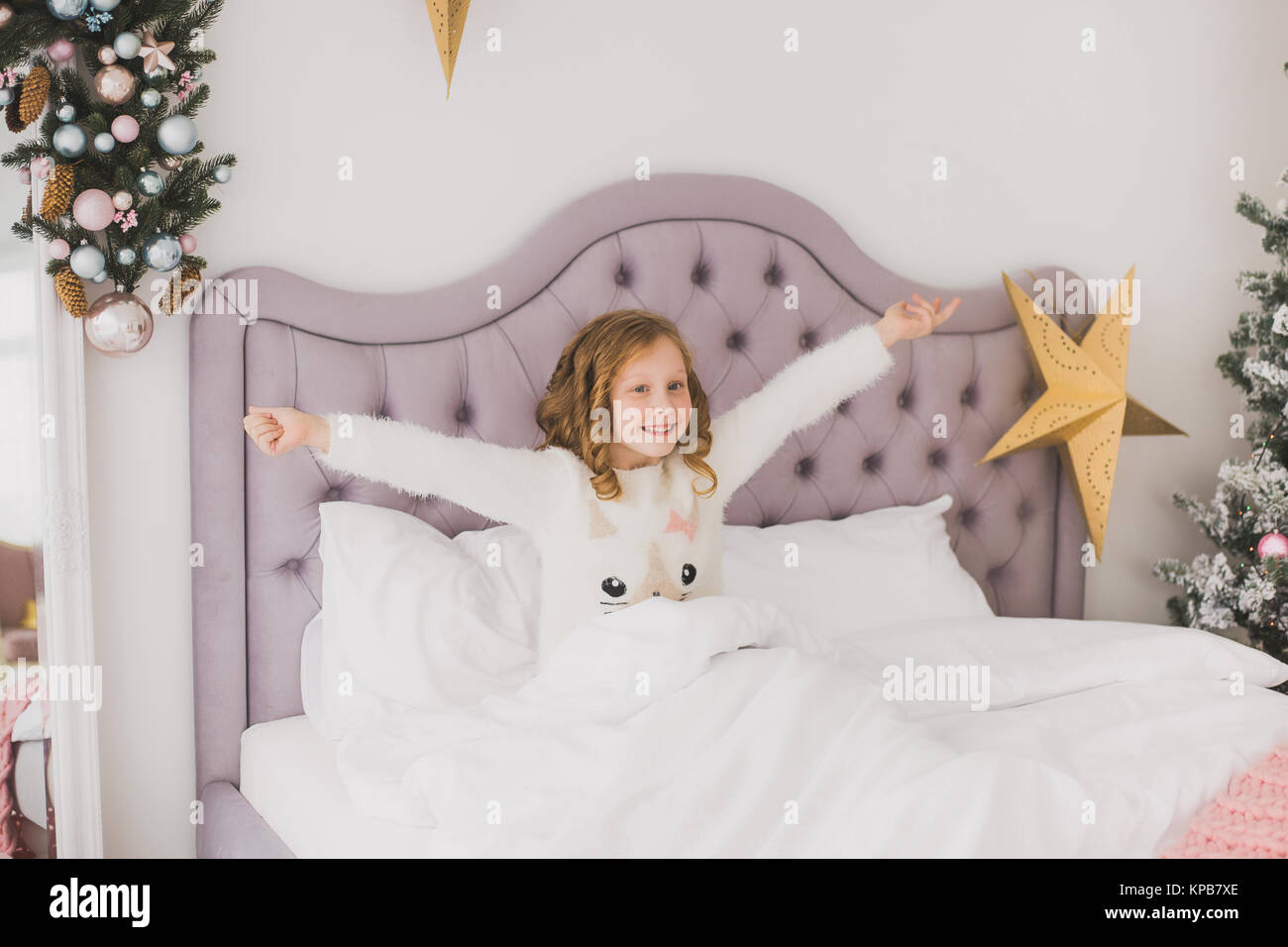 Portrait von niedlichen Lustige kleine Mädchen am Weihnachtsmorgen in Weiß Home Interior. Kind fröhlich im Bett sitzen. Horizontale Farbe Bild Stockfoto