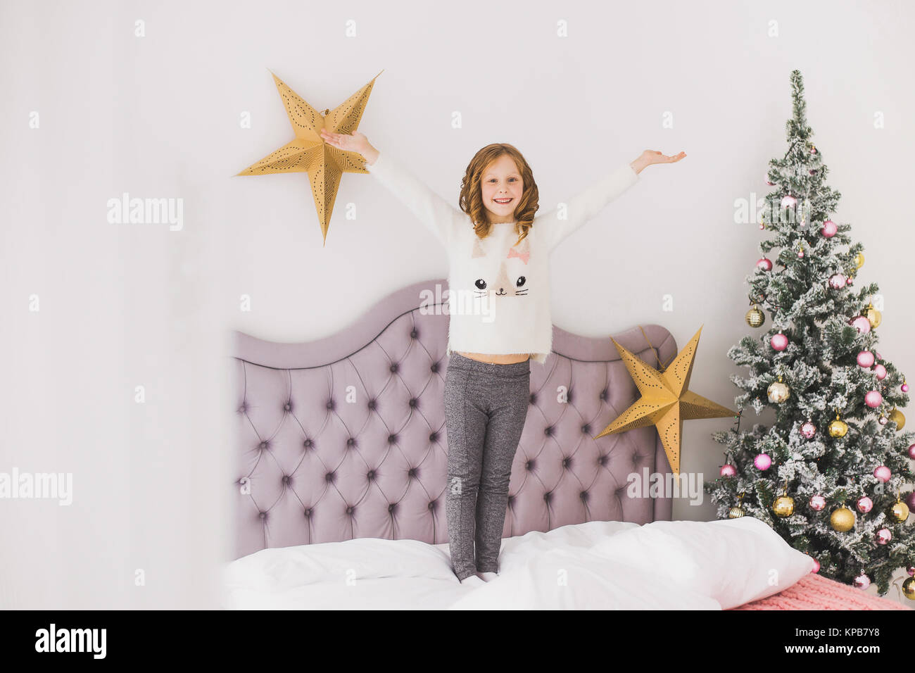 Portrait von niedlichen glücklichen kleinen Mädchen am Weihnachtsmorgen in Home Interior. Kind bezahlen mit Urlaub Dekoration bei der Verlegung auf dem Bett. Horizontale Farbe p Stockfoto