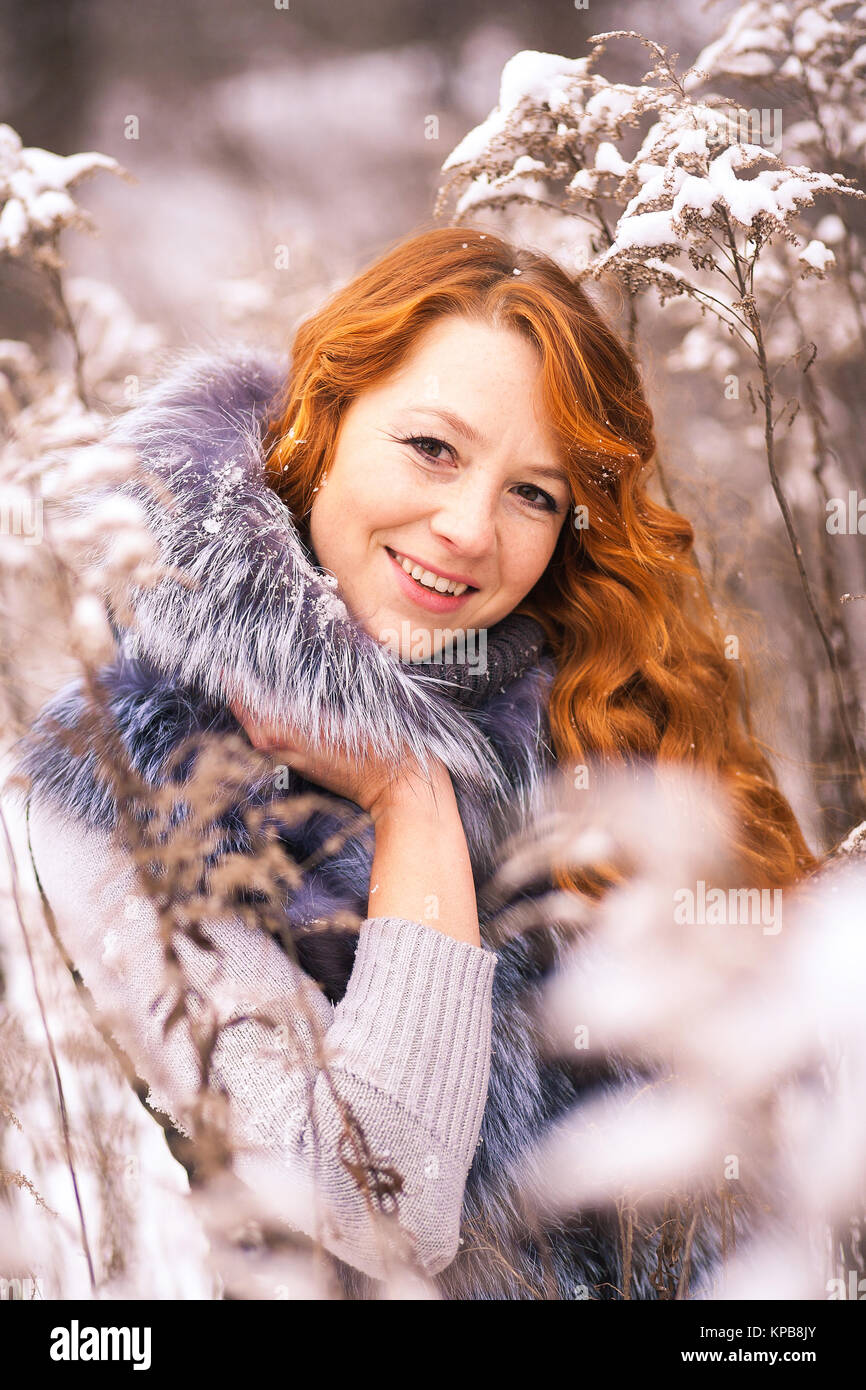 Porträt der schönen jungen Frau im Winter verschneite Wald Hintergrund. Nahaufnahme der weiblichen lächelndes Gesicht mit wunderschönen langen Ingwer Haar. Stockfoto