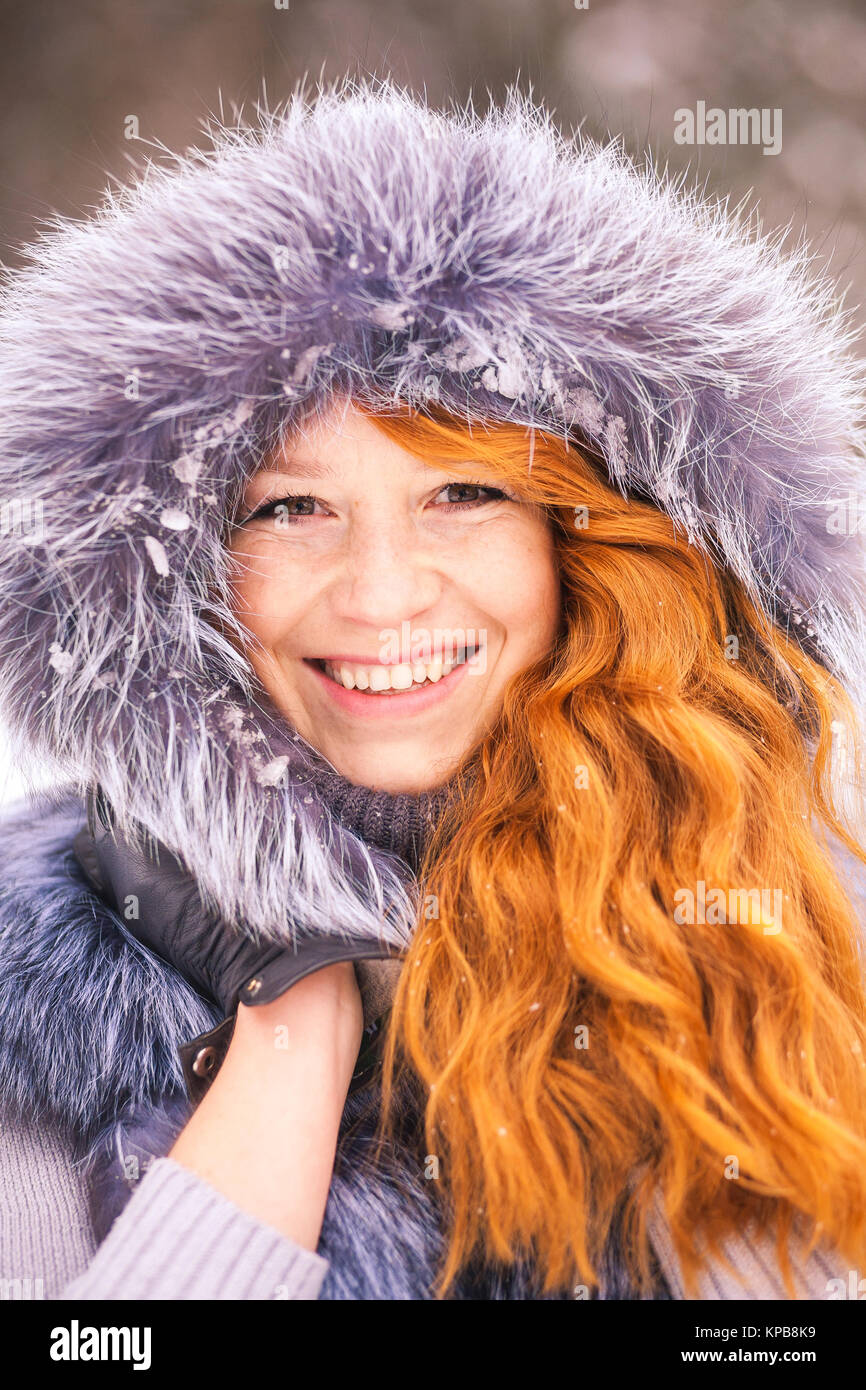Portrait von lächelnden ginger Winter Mädchen fröhlich in die Kamera schauen. Nahaufnahme von Schönheit Gesicht der jungen Frau im Winter Fell Kleidung draussen im verschneiten Co Stockfoto