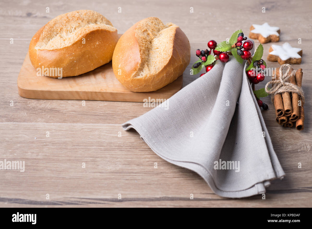 Frische Brötchen auf Schneidebrett mit Bettwäsche, Servietten und Weihnachtsschmuck Stockfoto