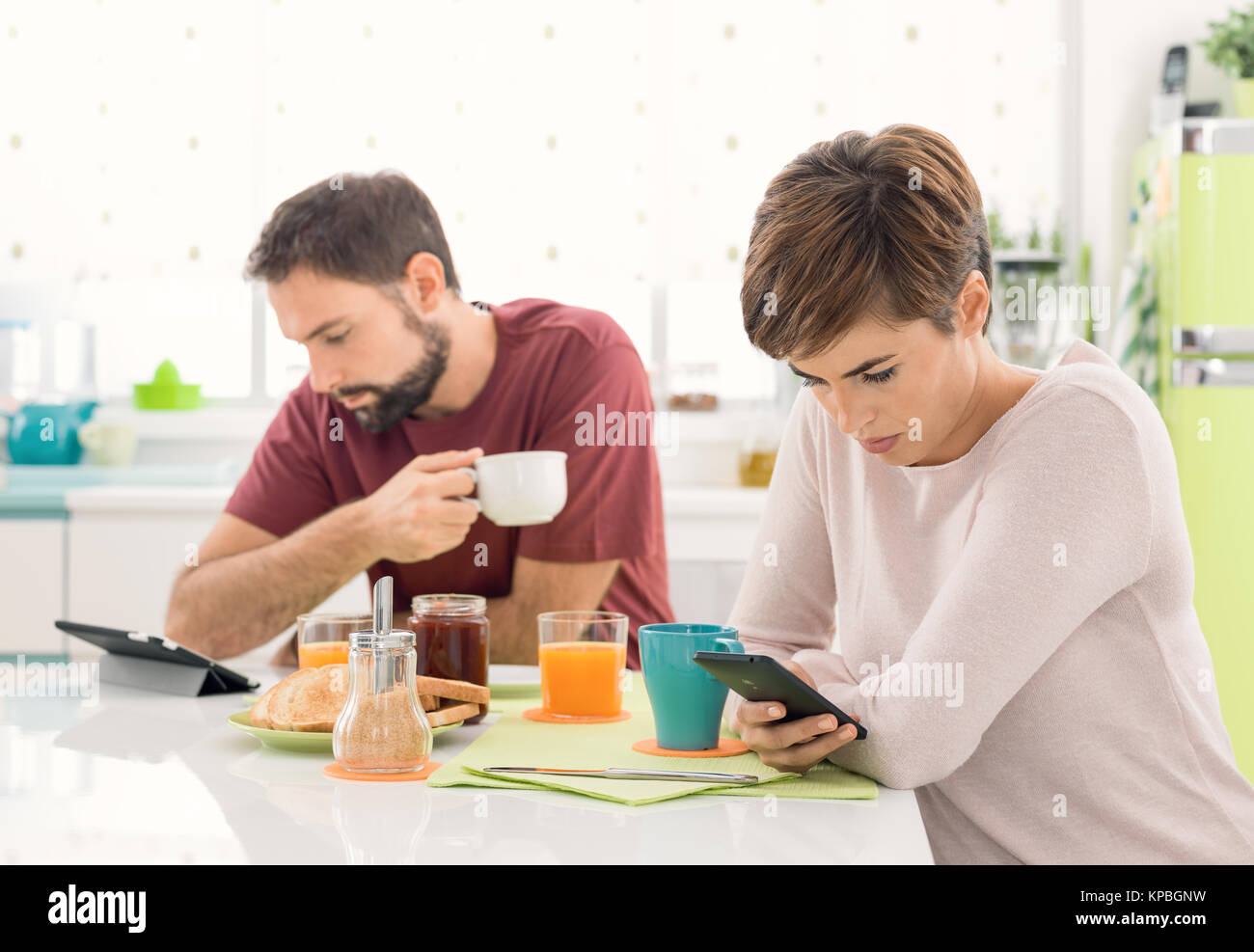 Junges Paar Frühstück zu Hause haben, werden Sie mit mobilen Geräten, Social Networking und zur Vermeidung von Wechselwirkungen: Neue Technologien und Soziale isolatio Stockfoto
