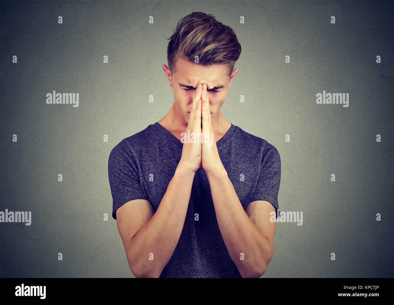Junger Mann Hand in Hand zusammen und berühren die Stirn beten mit starken Gefühlen halten die Augen geschlossen. Stockfoto