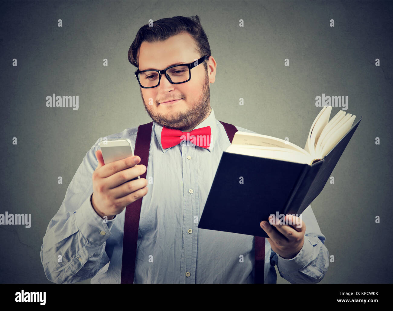 Junge fleischigen Mann, Buch, während bei der Verwendung von Smartphones auf grauem Hintergrund interessiert Stockfoto