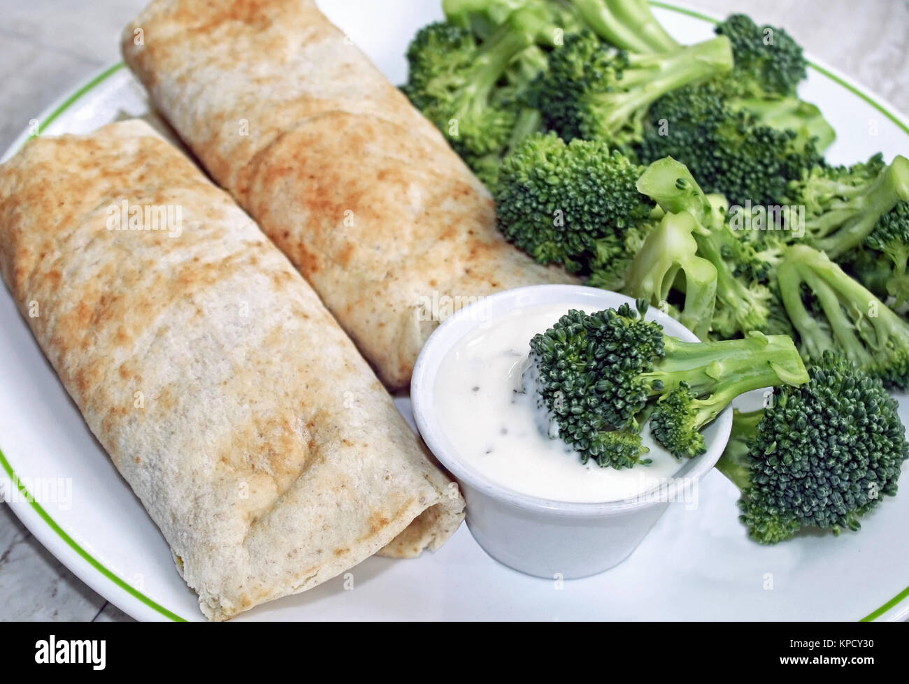 Zwei gefüllte Tortilla Wraps mit einer Seite der frischen Brokkoli und ein Container für cremige Dressing zum Dippen Stockfoto