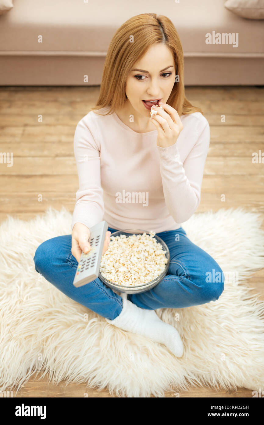 Fröhliche Frau in Jeans essen Popcorn auf dem Boden Stockfoto