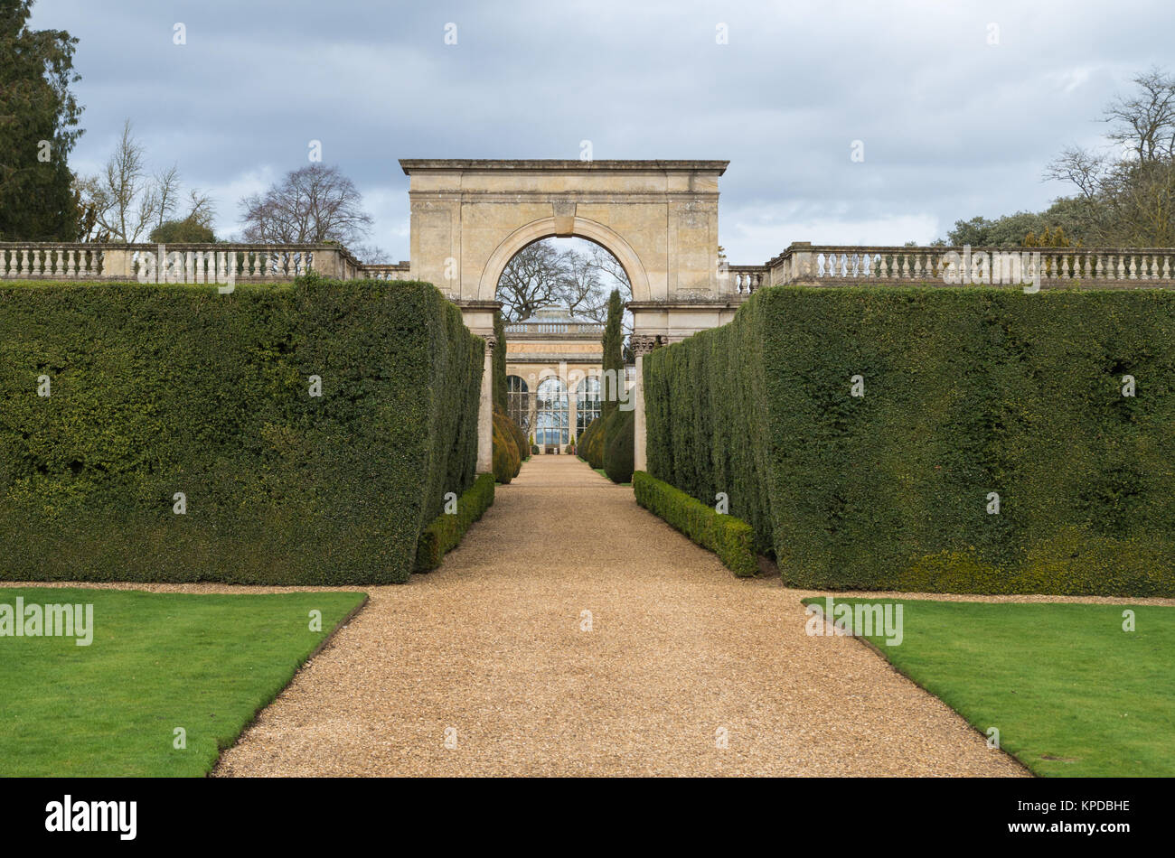 Kiesweg durch Hecken, die über einen Bogen zur Orangerie, Schloss Ashby Gärten, Großbritannien Stockfoto