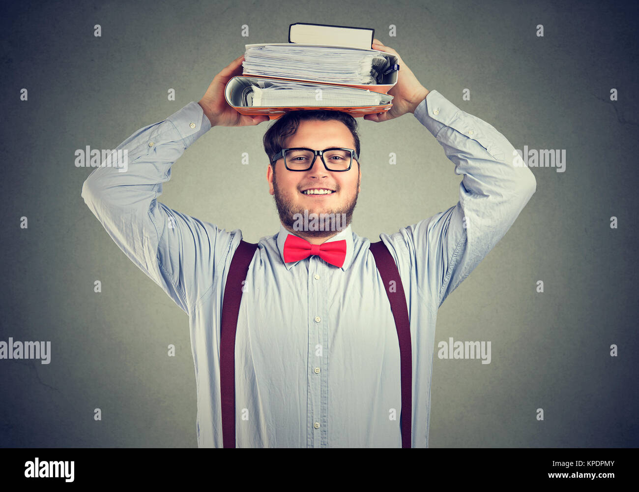 Chubby junger Mann in formelle Kleidung holding Haufen Lehrbücher auf den Kopf in die Kamera lächelt. Stockfoto