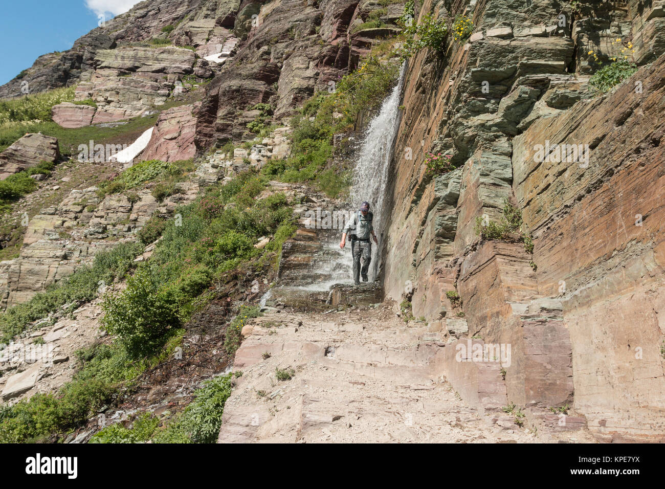 Ein Wanderer geht durch einen Wasserfall am Grinnell Glacier Trail im Glacier National Park, Montana Stockfoto