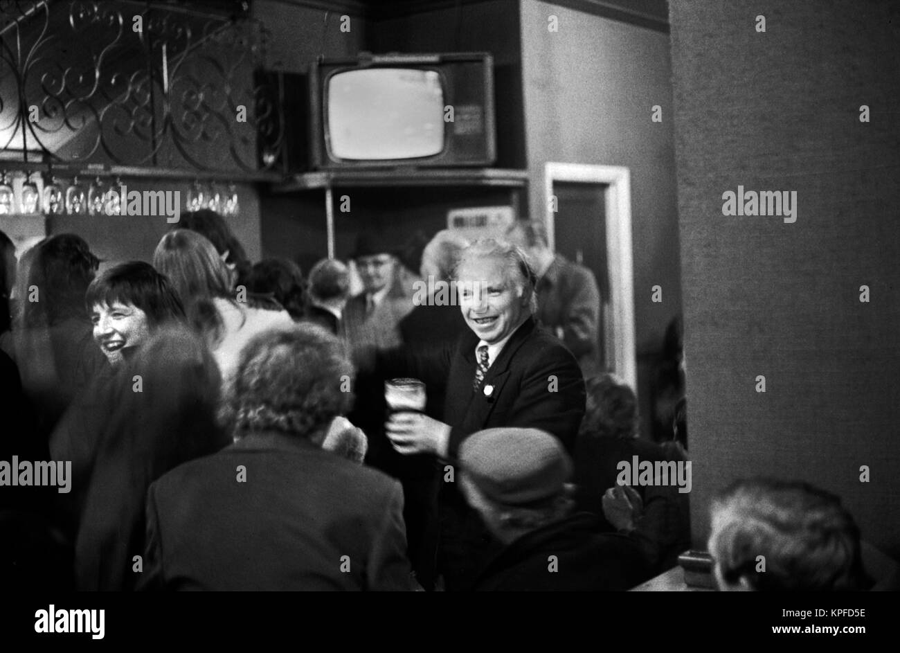 Londoner Pub aus den 1970er Jahren, voll mit Sonnentrinkern, Paar, die einen Witz teilen, lachen lächelnd. Ein Mann, der mit einem halben betrunkenen Pint Bier durch die Bar läuft. 70er London 1972 UK HOMER SYKES. Stockfoto