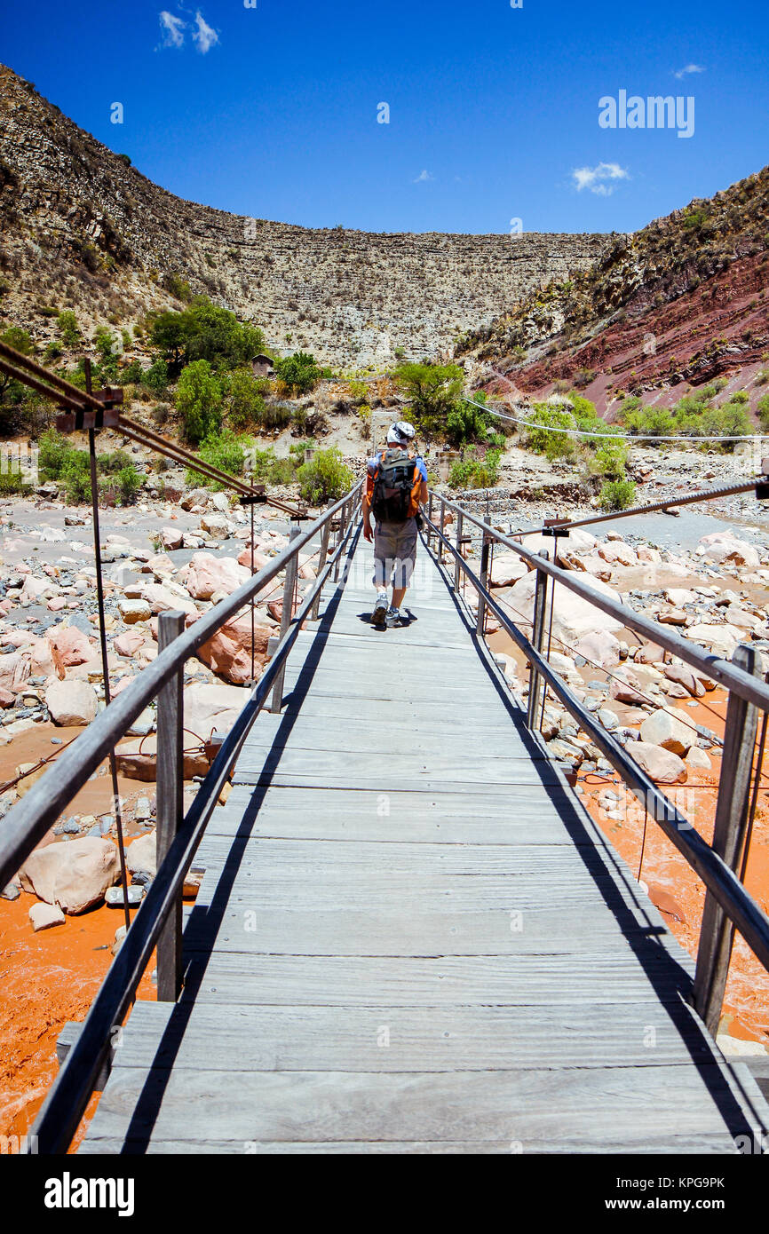 Ein Mann geht über eine Brücke über einen Red Mountain River in Bolivien Stockfoto