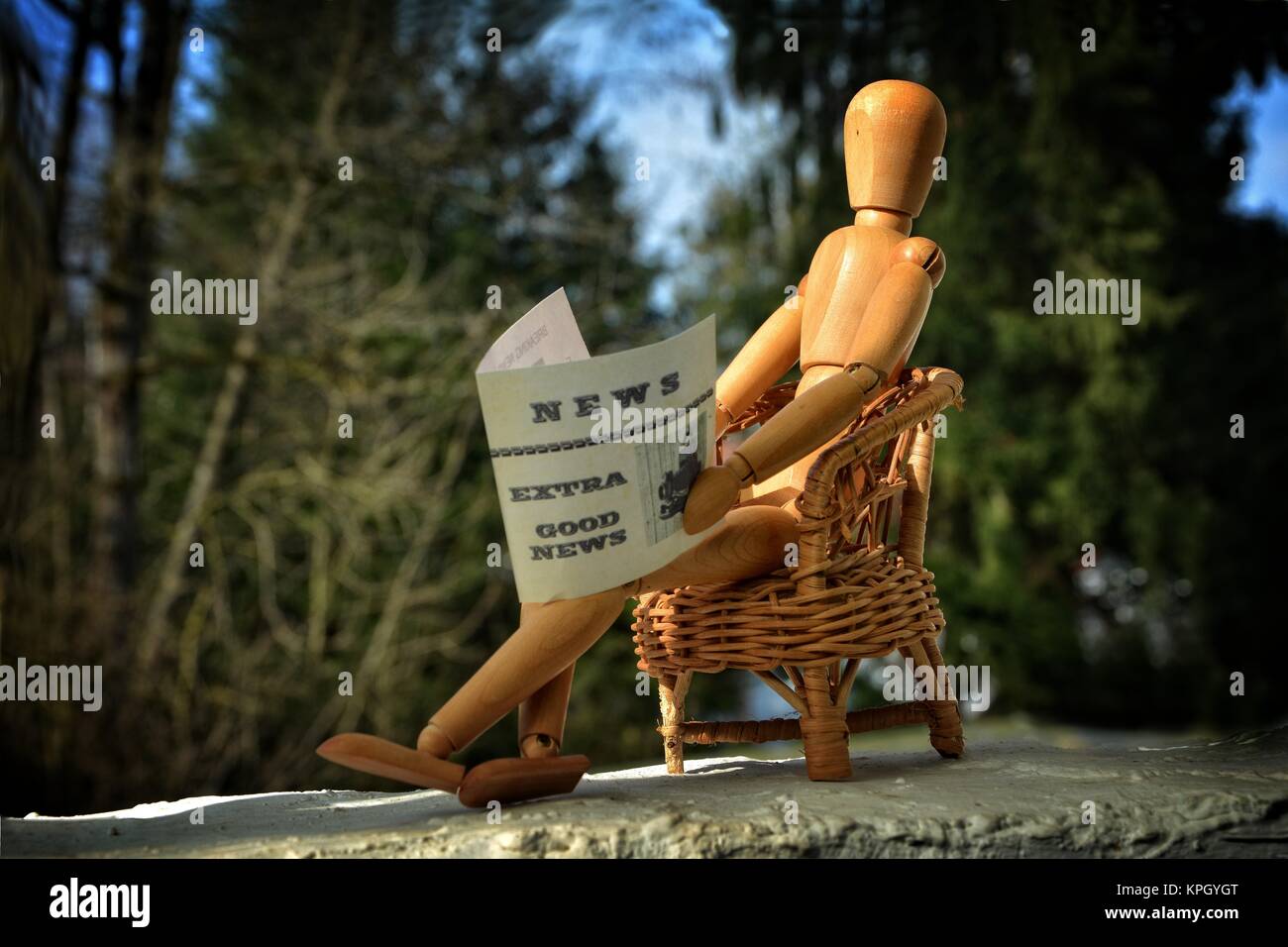 Holzfigur sitzt auf der Terrasse im Sessel und liest Zeitung Stockfoto