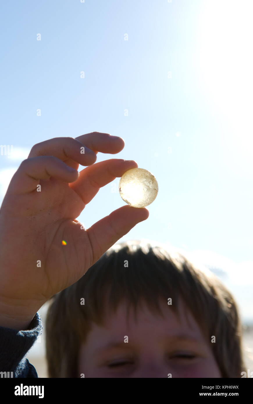 Ein acht Jahre alter Junge hält eine Marmor gefunden, die von der Sonne beleuchtet wird Stockfoto