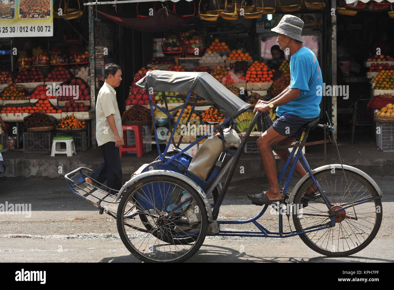 Ein cyclo oder Velo-rikscha Fahrten Vergangenheit 'Alter Markt', Open air Obst steht im Hintergrund, Phnom Penh, Kambodscha. Credit: Kraig Lieb Stockfoto