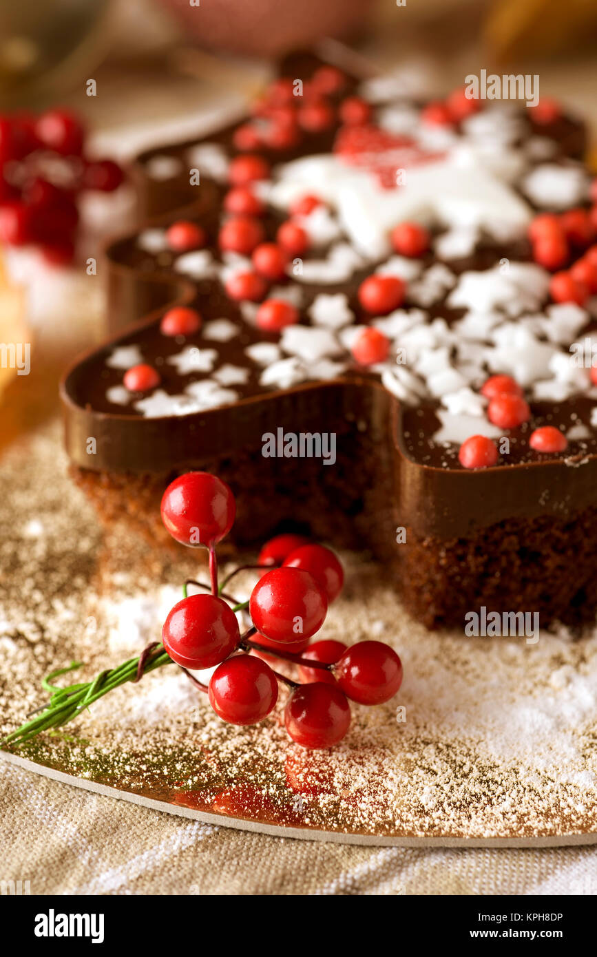Nahaufnahme einer Schokolade Kuchen in der Form eines Weihnachtsbaumes verziert mit sternförmigen besprüht und rote Beere-förmige Dragees, auf einem Tisch platziert wird eingestellt Stockfoto