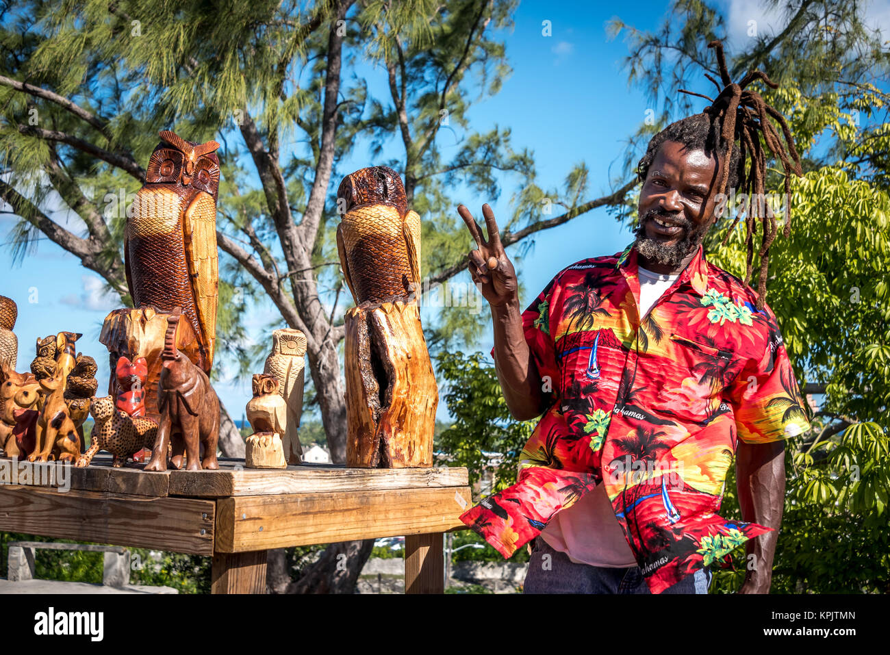 Ein lächelndes Holzschnitzer Handwerker mit geschnitzten Tiere auf Anzeige, Verkauf von Holz- Eulen, Elefant Schnitzereien an Touristen in der Nähe von Fincastle in Nassau, Bahamas Stockfoto