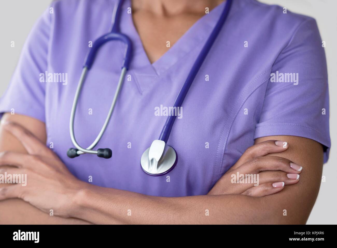 Ärztin in lila Top mit Stethoskop, die Arme verschränkt. Stockfoto