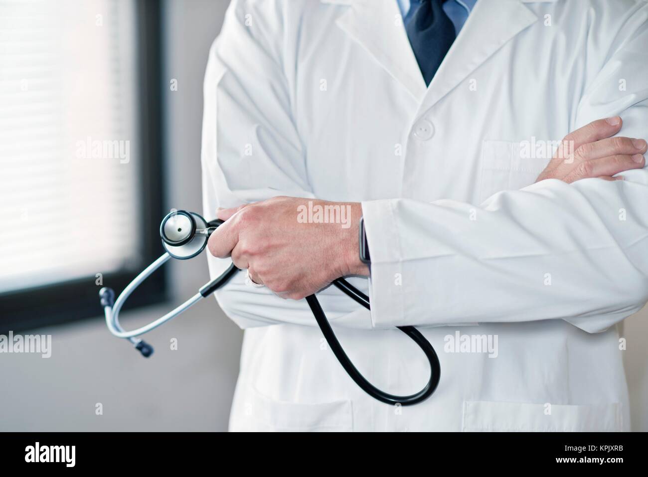 Männlicher Arzt im weißen Kittel mit Stethoskop, die Arme verschränkt. Stockfoto