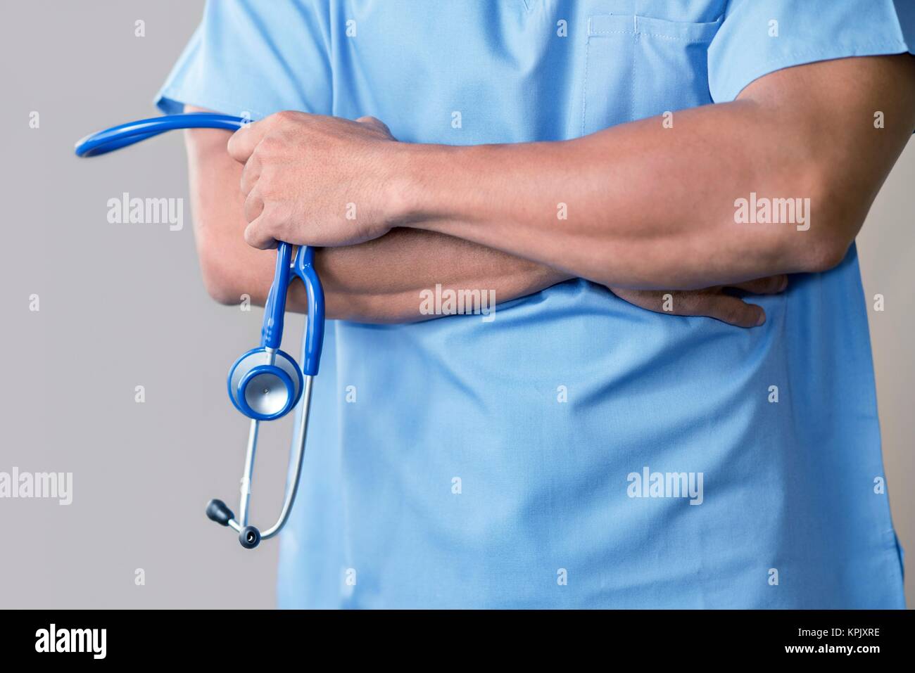 Männlicher Arzt in blauer Uniform mit Stethoskop, die Arme verschränkt. Stockfoto