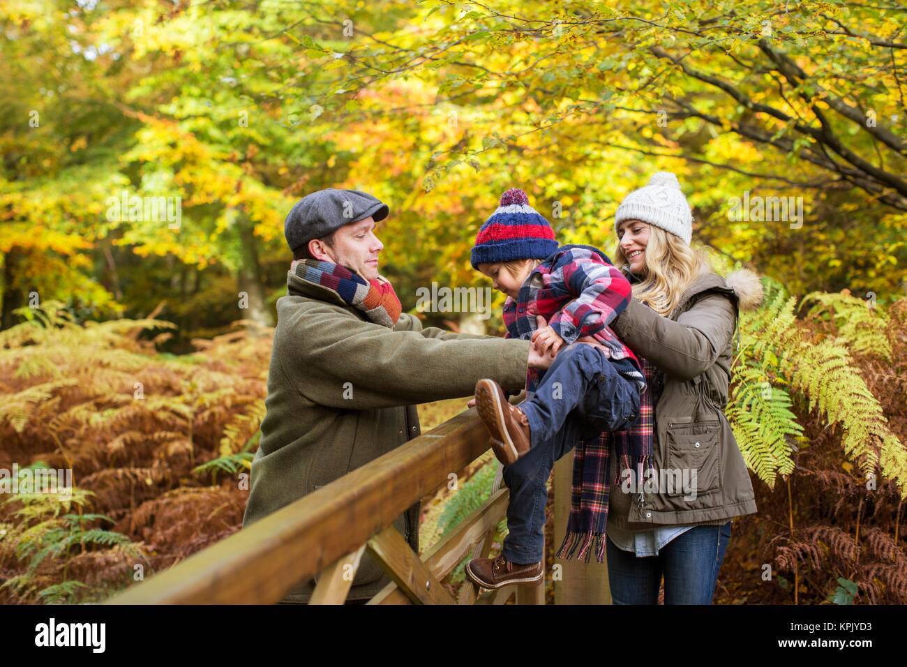 Familie im Wald im Herbst, die Mutter ihrem Sohn helfen, über ein Tor. Stockfoto