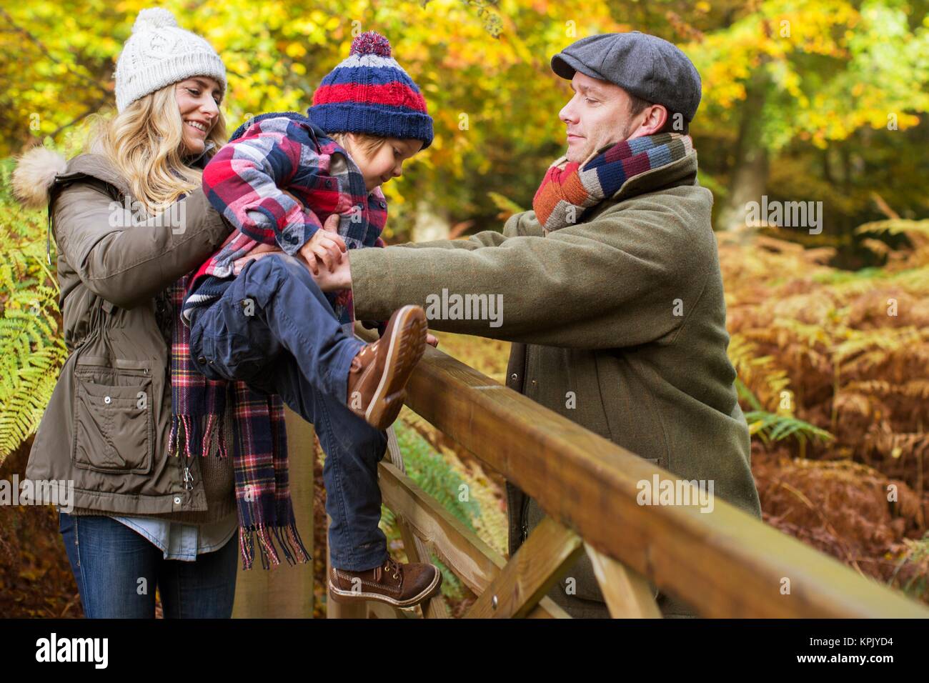 Familie im Wald im Herbst, die Mutter ihrem Sohn helfen, über ein Tor. Stockfoto