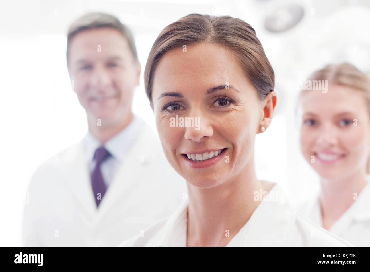 Ärztin in Richtung Kamera lächelnd, zwei Ärzte im Hintergrund. Stockfoto