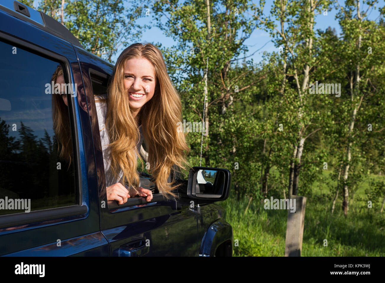 Eine schöne junge Frau mit langen blonden Haaren, die auf der Suche nach einem Fahrzeug Fenster und für die Kamera posieren; Edmonton, Alberta, Kanada Stockfoto